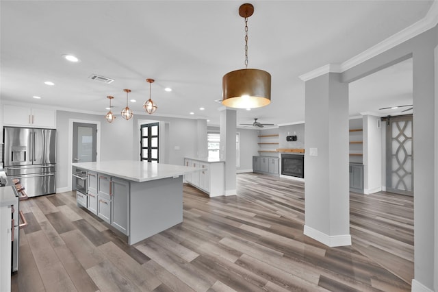 kitchen featuring pendant lighting, appliances with stainless steel finishes, white cabinetry, a center island, and ornamental molding