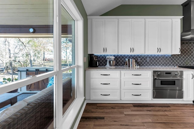 kitchen featuring dark hardwood / wood-style flooring, wall chimney range hood, oven, and white cabinets