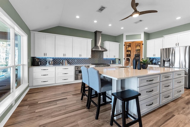 kitchen featuring white cabinetry, sink, a kitchen breakfast bar, a kitchen island with sink, and wall chimney range hood