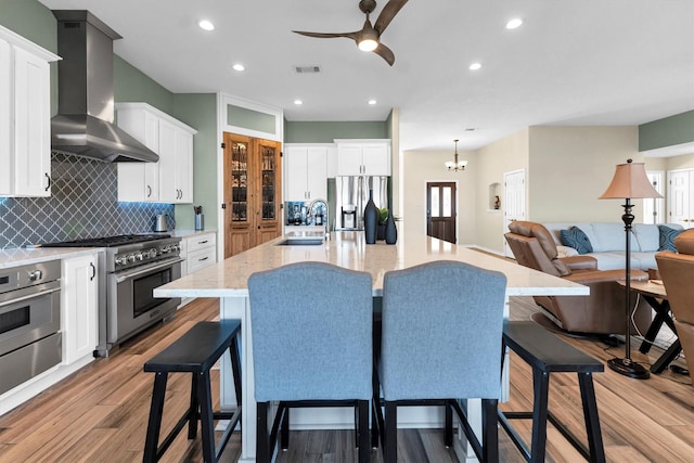 kitchen with a large island, sink, appliances with stainless steel finishes, white cabinetry, and wall chimney exhaust hood