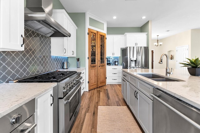 kitchen with appliances with stainless steel finishes, decorative light fixtures, white cabinetry, sink, and wall chimney range hood