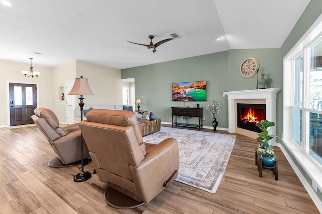 living room with ceiling fan with notable chandelier, vaulted ceiling, and light hardwood / wood-style floors