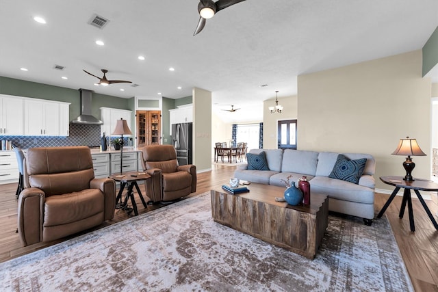 living room with ceiling fan with notable chandelier and light wood-type flooring