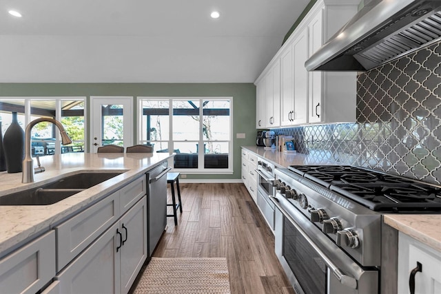 kitchen with sink, white cabinetry, stainless steel appliances, light stone countertops, and wall chimney exhaust hood