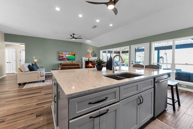 kitchen featuring dishwasher, sink, gray cabinetry, a kitchen island with sink, and light stone counters