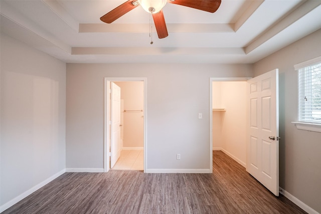 unfurnished bedroom featuring dark hardwood / wood-style flooring, a walk in closet, ceiling fan, a raised ceiling, and ensuite bath