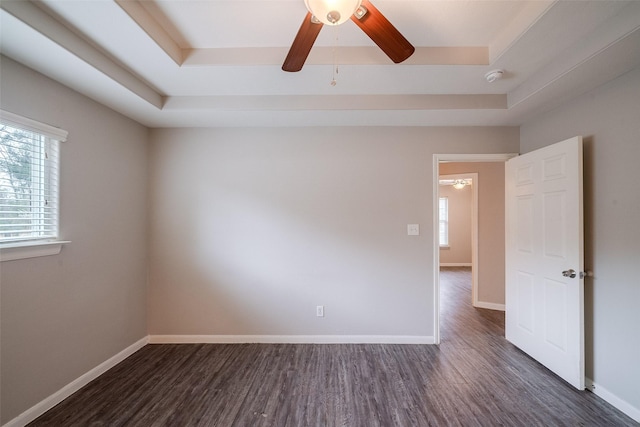 empty room with dark wood-type flooring, a raised ceiling, and ceiling fan