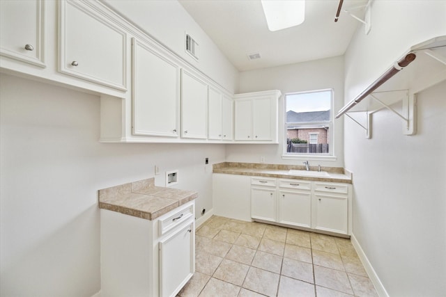 kitchen with light tile patterned floors, a sink, visible vents, white cabinetry, and baseboards