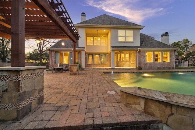 back house at dusk featuring pool water feature, a pergola, and a patio