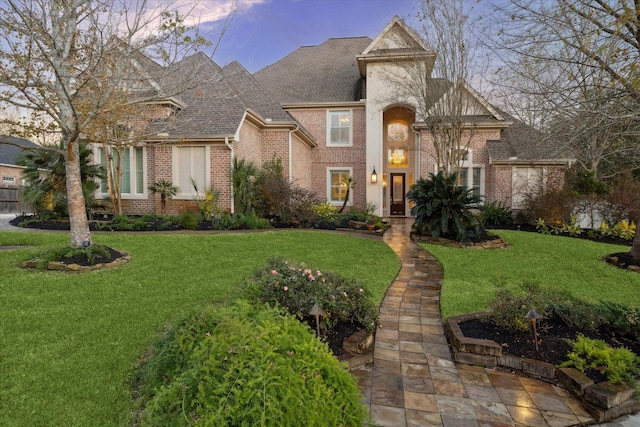 view of front of property featuring brick siding, roof with shingles, and a front yard