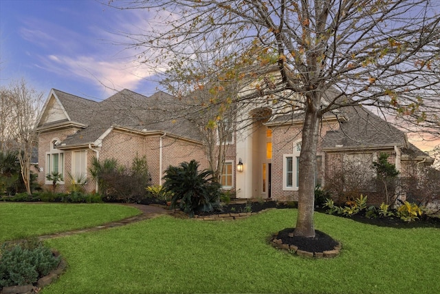 view of front of house with a front lawn, roof with shingles, and brick siding