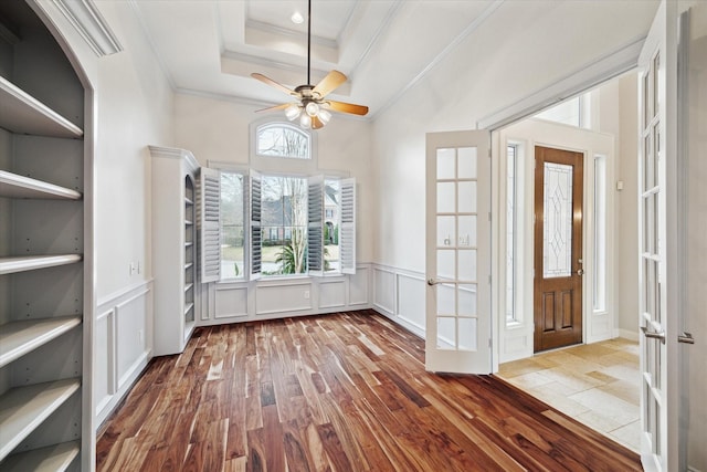 interior space with a raised ceiling, crown molding, ceiling fan, and light wood-type flooring