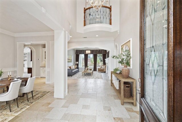 foyer featuring arched walkways, ornamental molding, an inviting chandelier, a high ceiling, and stone tile flooring