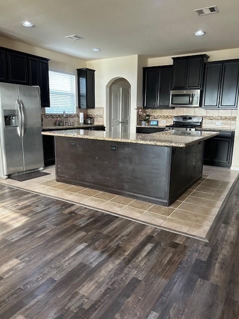 kitchen featuring a kitchen island, tasteful backsplash, light stone counters, light hardwood / wood-style floors, and stainless steel appliances