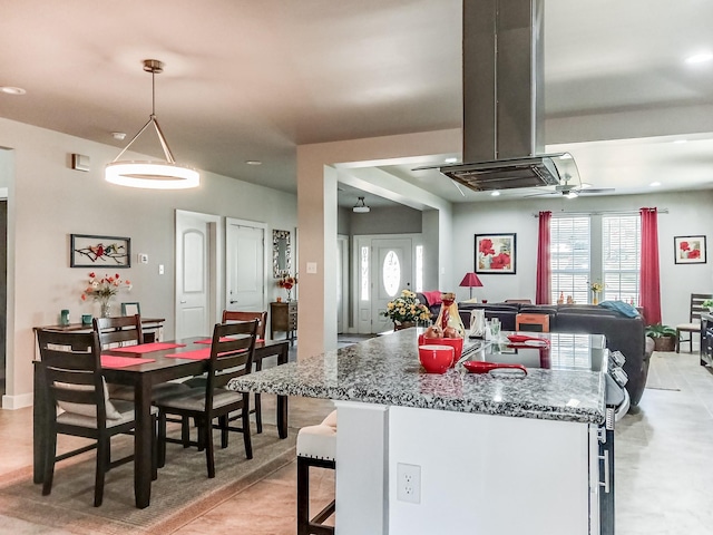 kitchen featuring island exhaust hood, a breakfast bar area, stone countertops, decorative light fixtures, and ceiling fan