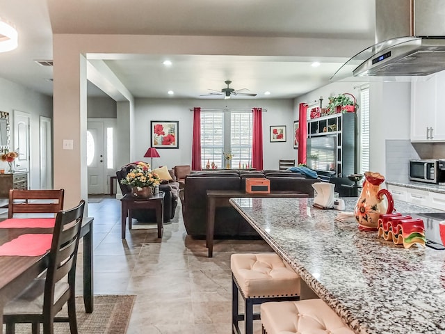 kitchen featuring a breakfast bar, island range hood, white cabinets, light tile patterned floors, and light stone countertops