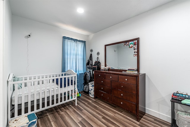 bedroom with dark wood-type flooring and a crib