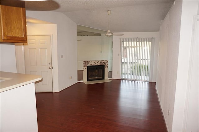 unfurnished living room featuring lofted ceiling, a textured ceiling, dark hardwood / wood-style flooring, ceiling fan, and a tiled fireplace