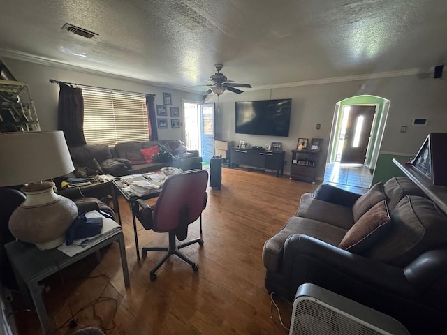 living room with ceiling fan, crown molding, wood-type flooring, and a textured ceiling