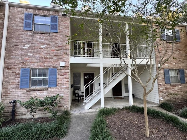 back of house with brick siding, a patio, and stairway