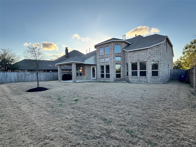 back house at dusk featuring a yard and a patio