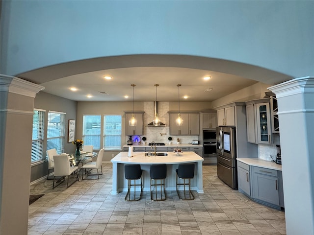 kitchen featuring appliances with stainless steel finishes, pendant lighting, tasteful backsplash, sink, and wall chimney exhaust hood