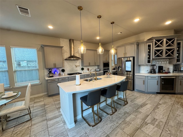 kitchen featuring a kitchen bar, sink, hanging light fixtures, appliances with stainless steel finishes, and wall chimney range hood