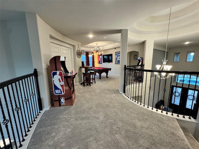 corridor featuring an inviting chandelier, a raised ceiling, and carpet