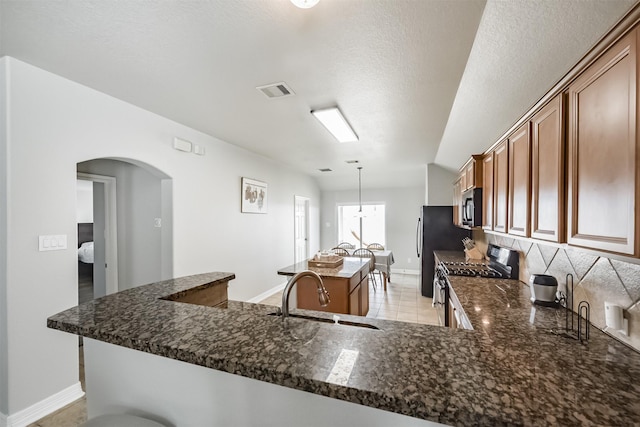 kitchen with sink, dark stone countertops, decorative light fixtures, stainless steel range with gas cooktop, and kitchen peninsula