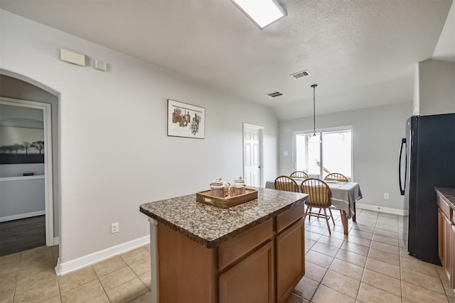 kitchen featuring black refrigerator, decorative light fixtures, lofted ceiling, a center island, and light tile patterned floors