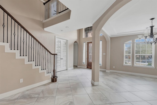 entrance foyer with crown molding, a notable chandelier, a towering ceiling, and light tile patterned floors