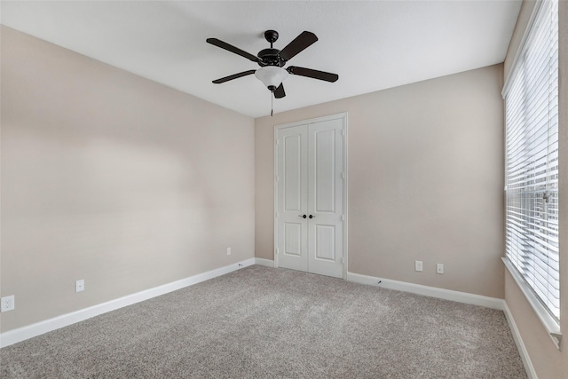 unfurnished bedroom featuring multiple windows, carpet floors, ceiling fan, and a closet