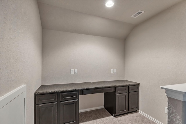 unfurnished office with lofted ceiling, built in desk, and light colored carpet