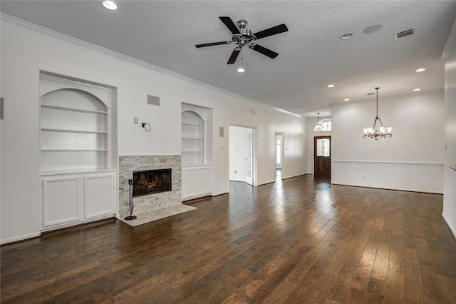 unfurnished living room with crown molding, dark wood-type flooring, ceiling fan with notable chandelier, a tiled fireplace, and built in shelves