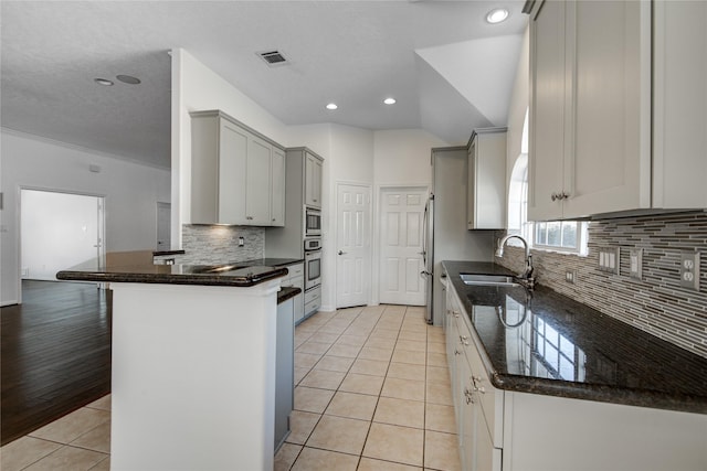 kitchen with sink, stainless steel appliances, light tile patterned flooring, kitchen peninsula, and dark stone counters