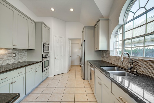 kitchen with light tile patterned flooring, sink, dark stone countertops, stainless steel appliances, and backsplash