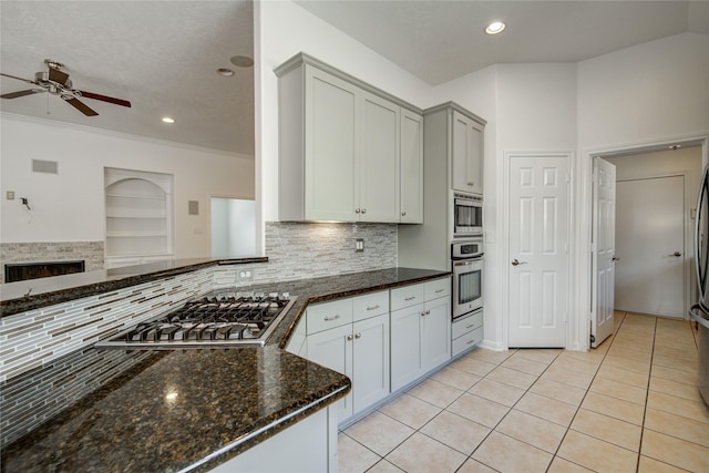 kitchen with light tile patterned floors, crown molding, appliances with stainless steel finishes, backsplash, and dark stone counters