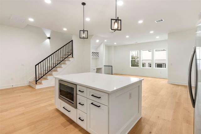 kitchen featuring pendant lighting, appliances with stainless steel finishes, a center island, light hardwood / wood-style floors, and white cabinets