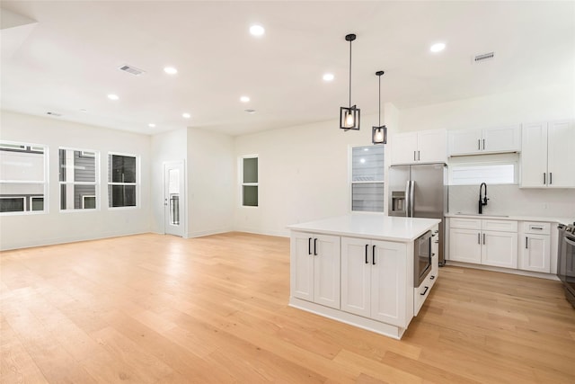 kitchen with sink, white cabinetry, a center island, light hardwood / wood-style flooring, and pendant lighting