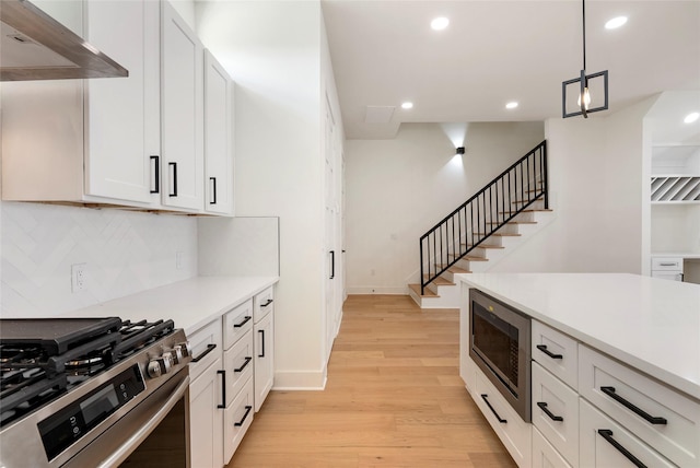 kitchen featuring stainless steel appliances, white cabinets, light hardwood / wood-style floors, and decorative light fixtures