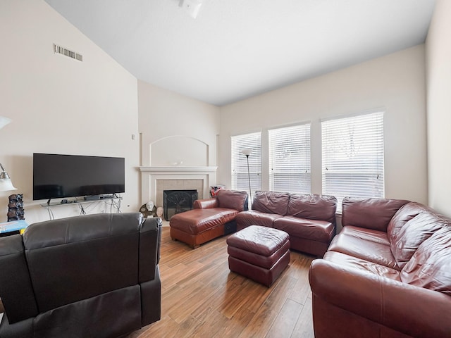 living room featuring hardwood / wood-style flooring, lofted ceiling, and a tiled fireplace