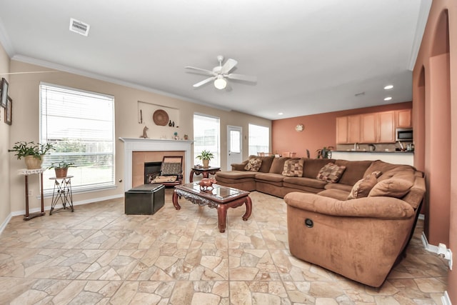 living room featuring a tiled fireplace, crown molding, and ceiling fan