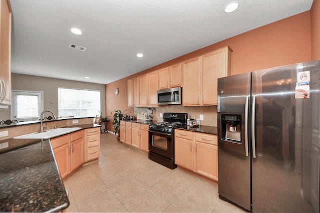 kitchen with appliances with stainless steel finishes, light brown cabinetry, backsplash, dark stone counters, and light tile patterned floors