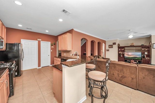 kitchen featuring sink, black gas stove, dark stone countertops, a kitchen bar, and kitchen peninsula