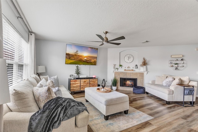 living room featuring a tiled fireplace, hardwood / wood-style floors, a textured ceiling, and ceiling fan