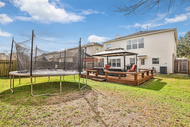 rear view of house featuring a lawn, a wooden deck, a trampoline, a gazebo, and central AC