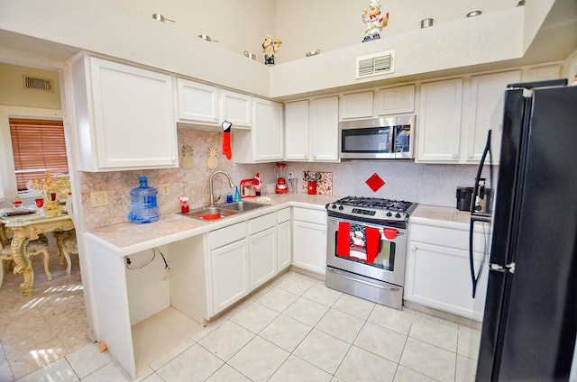 kitchen with sink, light tile patterned floors, stainless steel appliances, white cabinets, and decorative backsplash