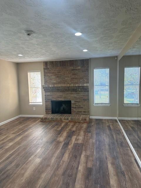 unfurnished living room with a brick fireplace, dark hardwood / wood-style floors, and a textured ceiling