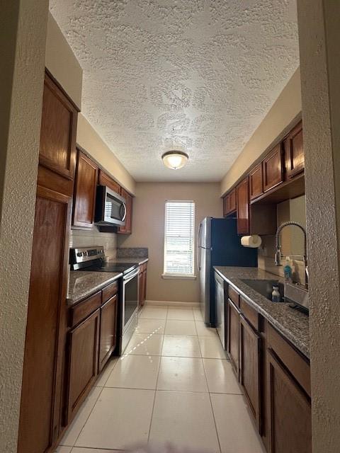 kitchen featuring appliances with stainless steel finishes, sink, decorative backsplash, light tile patterned floors, and a textured ceiling