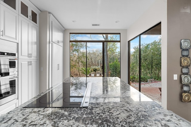 kitchen featuring white cabinetry, black electric stovetop, light stone countertops, and stainless steel double oven